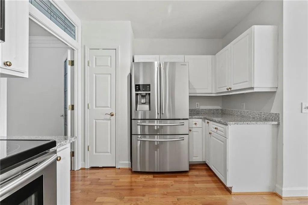 Kitchen featuring stainless steel appliances, white cabinetry, light wood-style floors, and light stone counters