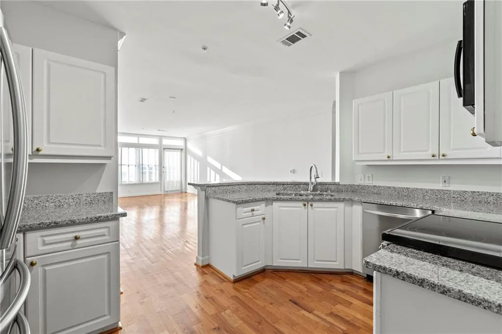 Kitchen with white cabinets, light wood finished floors, dishwasher, light stone countertops, and a peninsula