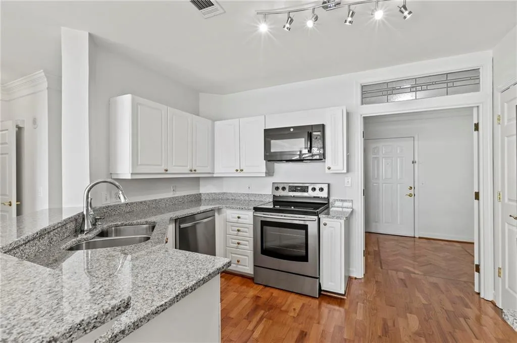 Kitchen with stainless steel appliances, white cabinetry, light stone counters, and light wood finished floors
