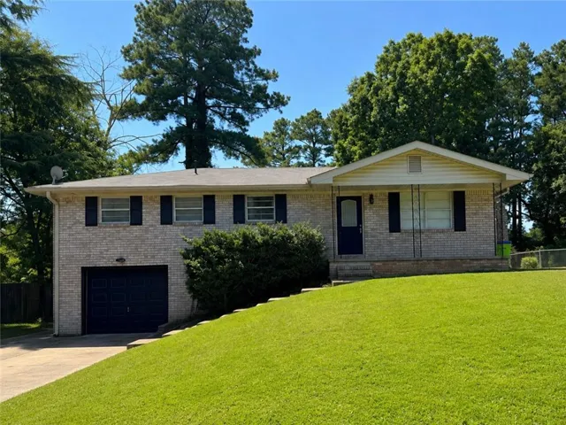 Brick split-level home featuring a two-car garage, multiple windows with black shutters, and a pitched roofline