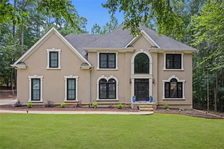 Stucco exterior with a prominent arched window, dark framed windows, a gabled roofline, and a stone-step entry