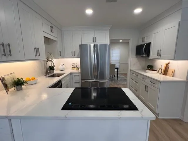 Kitchen featuring black appliances, light stone countertops, light wood-style flooring, a peninsula, and white cabinetry