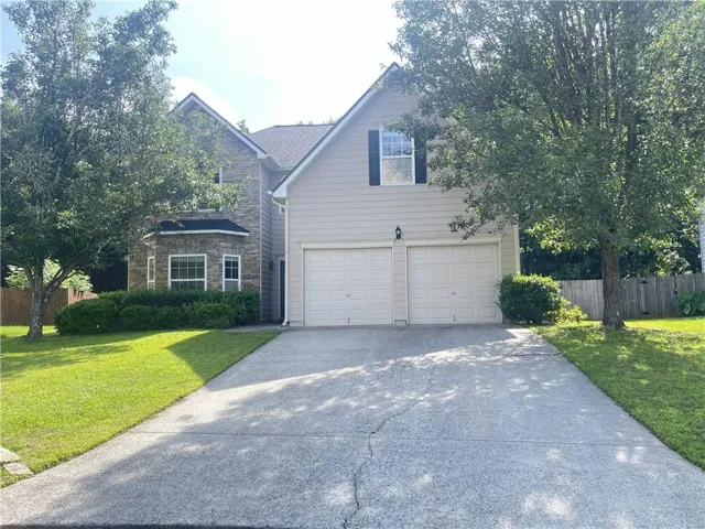Two-story residence featuring a combination of siding and stone veneer, a dual garage, a paved driveway, and mature trees framing the property