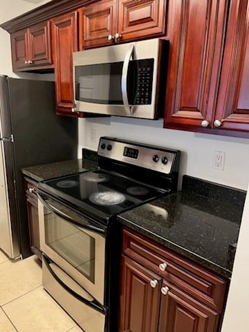 Kitchen with light tile floors, dark stone countertops, and appliances with stainless steel finishes