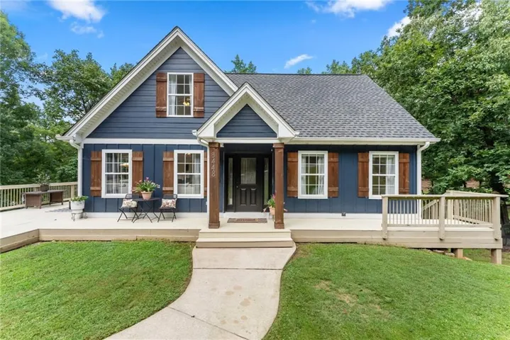 Classic farmhouse design featuring a deep navy exterior with contrasting white trim, a welcoming covered front porch with tapered columns, and a peaked gable roof with architectural detailing
