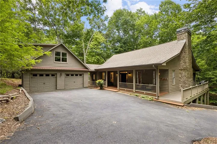 Wood-sided exterior featuring a two-car garage with carriage-style doors, a stone chimney, and a full-length covered porch