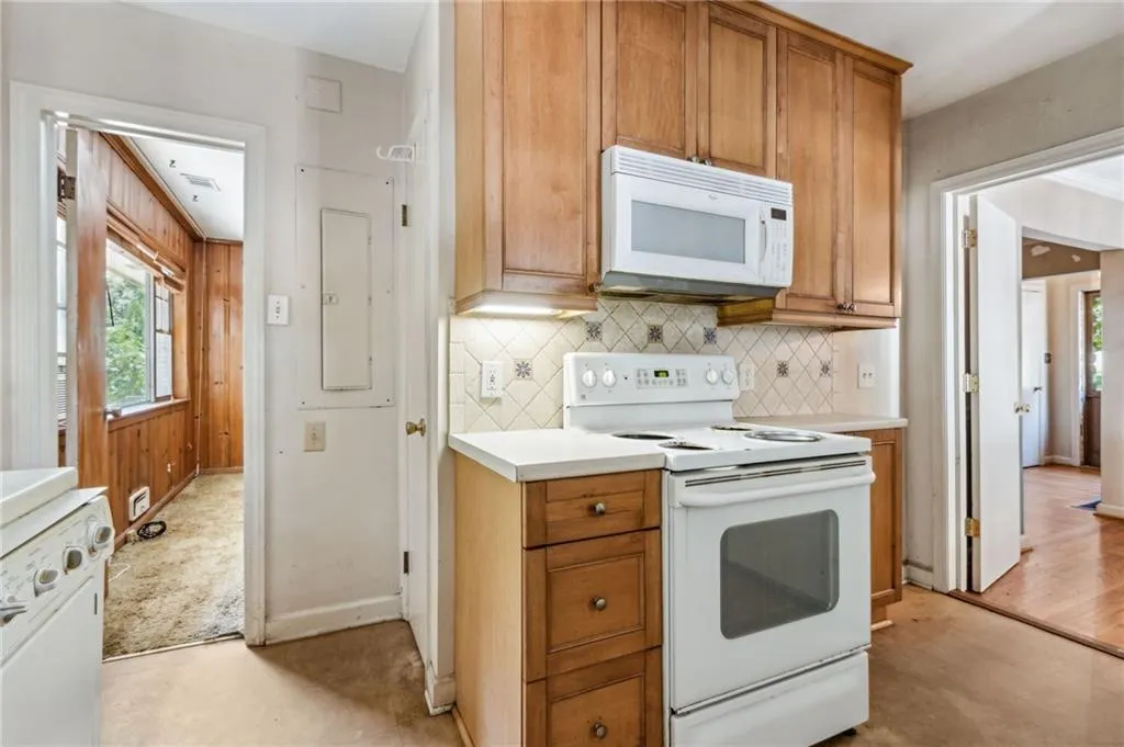 Kitchen featuring healthy amount of natural light, white appliances, light countertops, electric panel, and ornamental molding