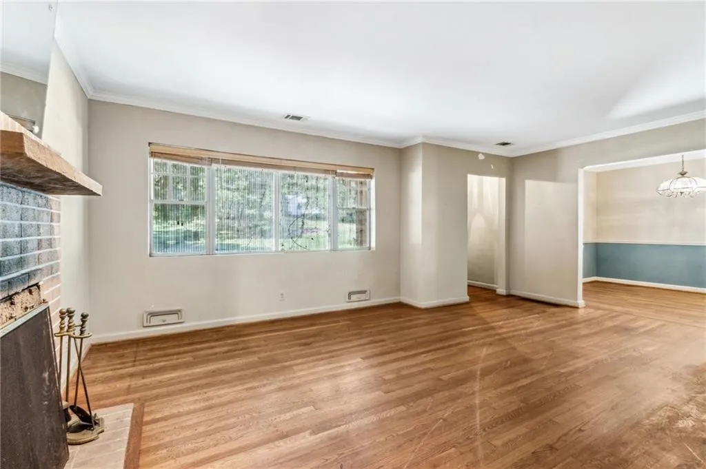 Wonderful view of living room window area with custom shades, crown molding, light wood-style flooring, a brick fireplace, and a chandelier