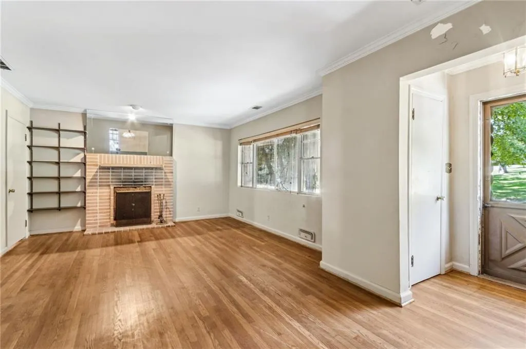 Living room featuring ornamental molding, wall shelving, light wood finished floors, and a brick fireplace
