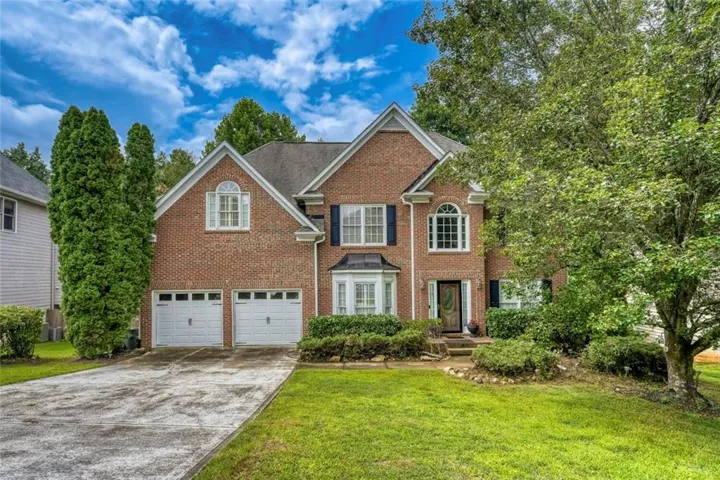 Traditional brick residence featuring a two-car garage, multiple gabled rooflines, and a bay window