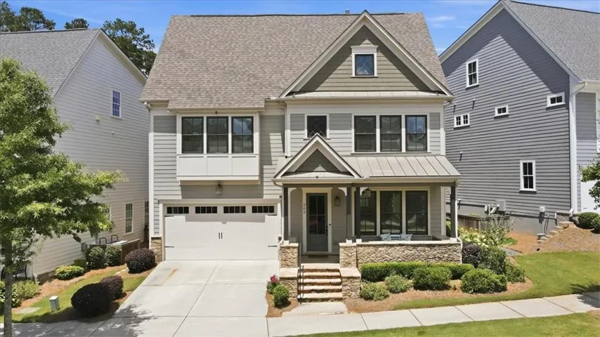 Two-story residence featuring a covered front porch with stone pillars, a two-car garage, and upper-level bay windows