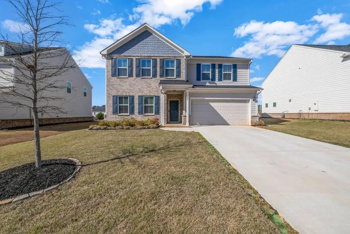 View of front of home featuring an attached garage, concrete driveway, a front lawn, and brick siding