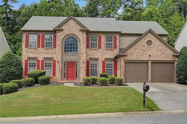 Two-story traditional brick home featuring a prominent arched window, red front door, and red window shutters