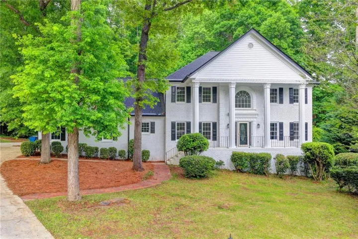 White brick exterior featuring a prominent portico with four columns, a central arched window, and a dark shingle roof
