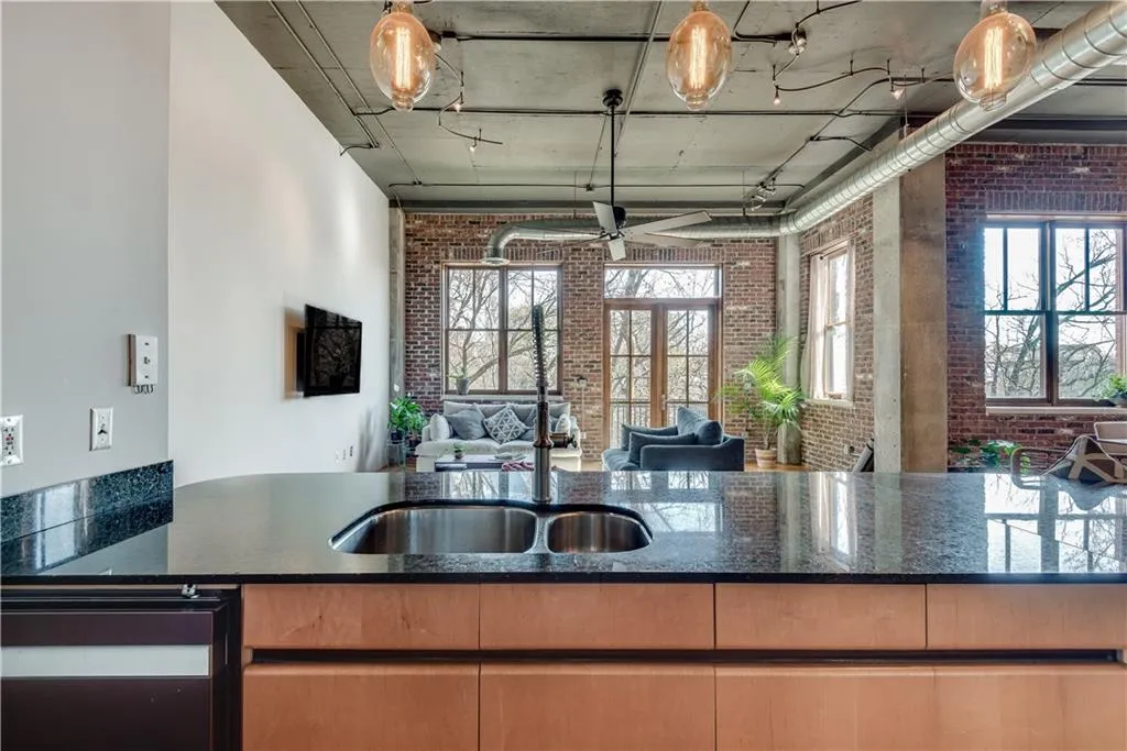 Kitchen with brick wall, dark stone counters, dishwashing machine, open floor plan, and healthy amount of natural light