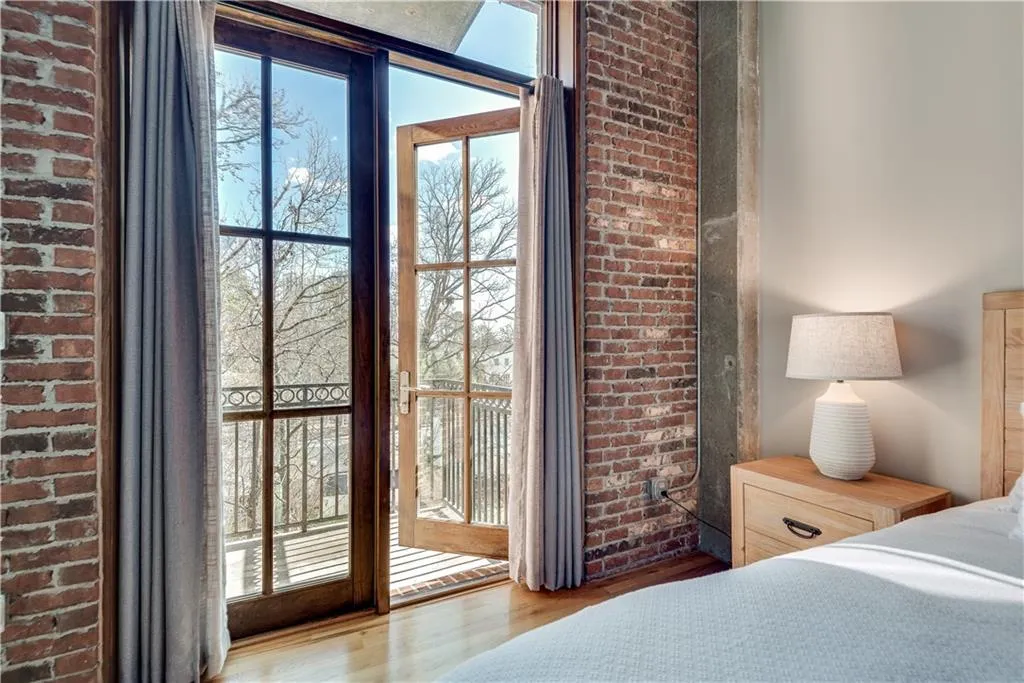 Bedroom with wood finished floors, brick wall, and access to outside