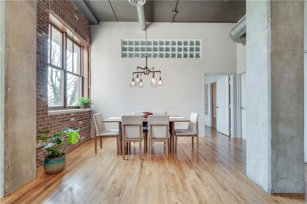Dining room with light wood finished floors, a towering ceiling, a chandelier, and brick wall