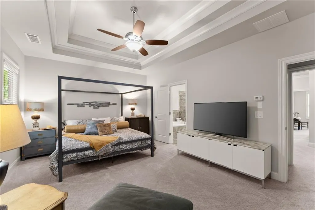 Bedroom with a tray ceiling, carpet, ceiling fan, and ornamental molding