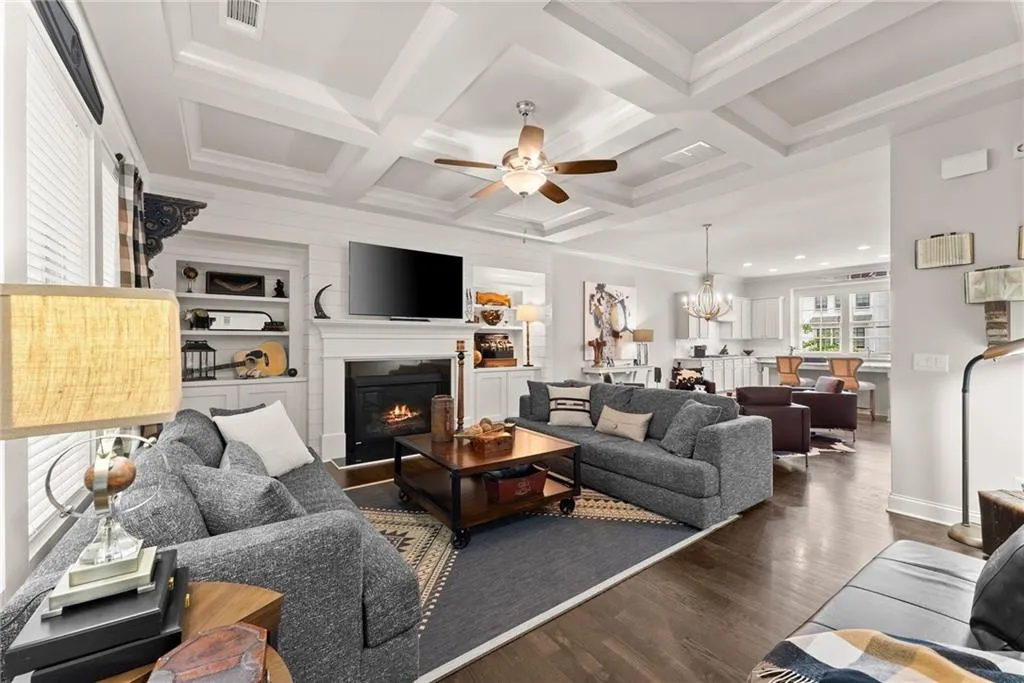 Living area with a glass covered fireplace, a ceiling fan, wood finished floors, crown molding, and a chandelier