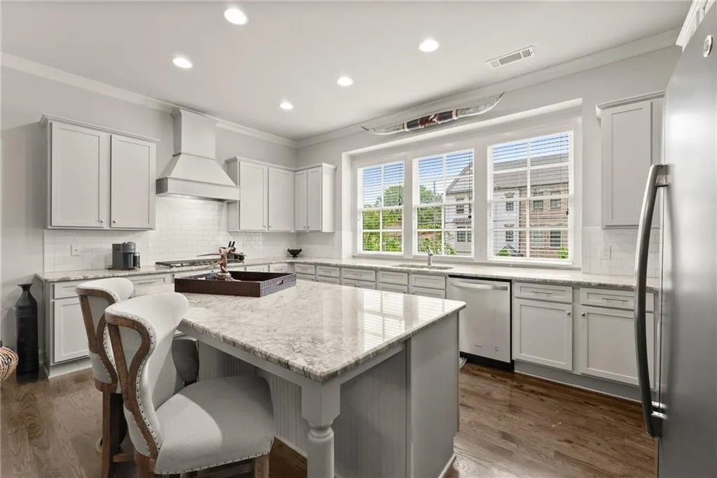 Kitchen featuring crown molding, light stone counters, decorative backsplash, stainless steel appliances, and white cabinets