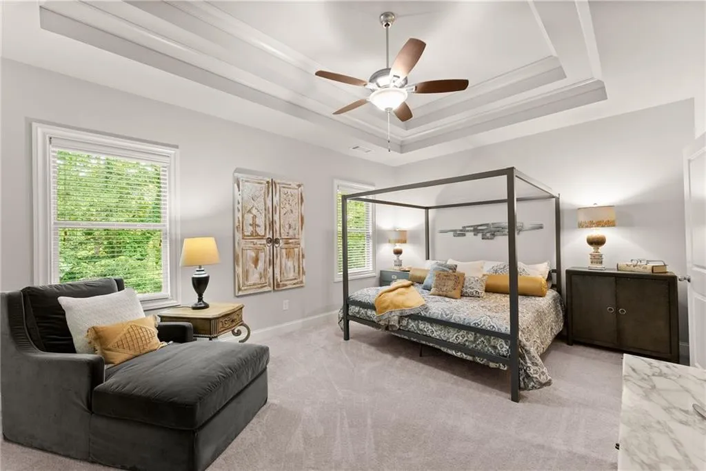 Carpeted bedroom featuring a tray ceiling and a ceiling fan