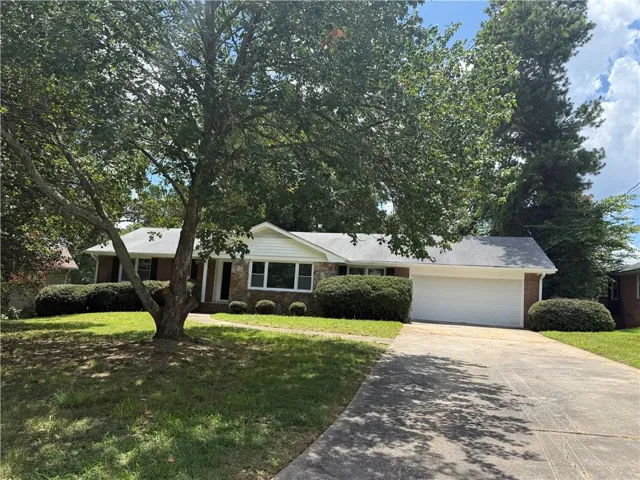 Ranch-style residence featuring a brick and white siding exterior, a two-car garage, a concrete driveway, a mature front yard tree, and established perimeter shrubbery