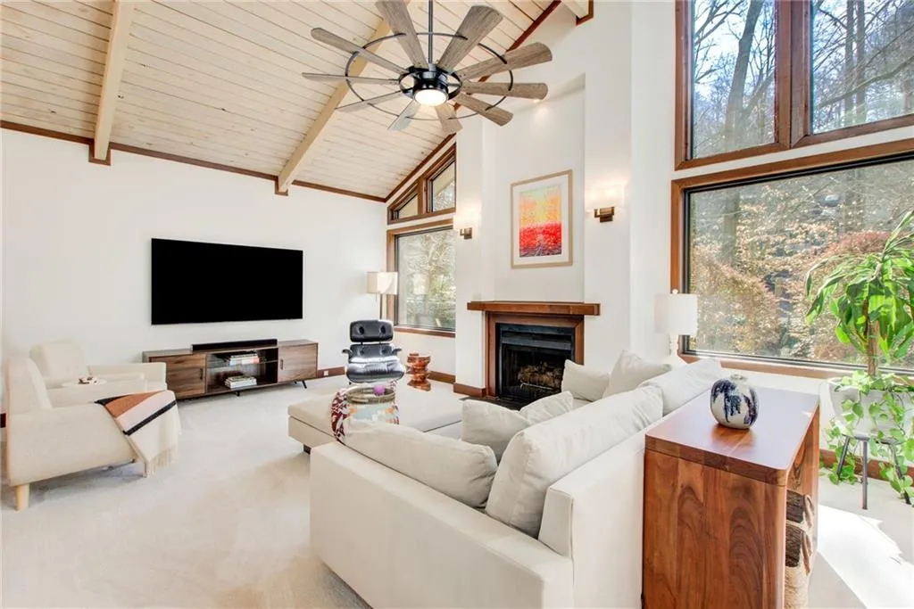 Carpeted living room with a fireplace, a ceiling fan, and a high wooden beamed ceiling