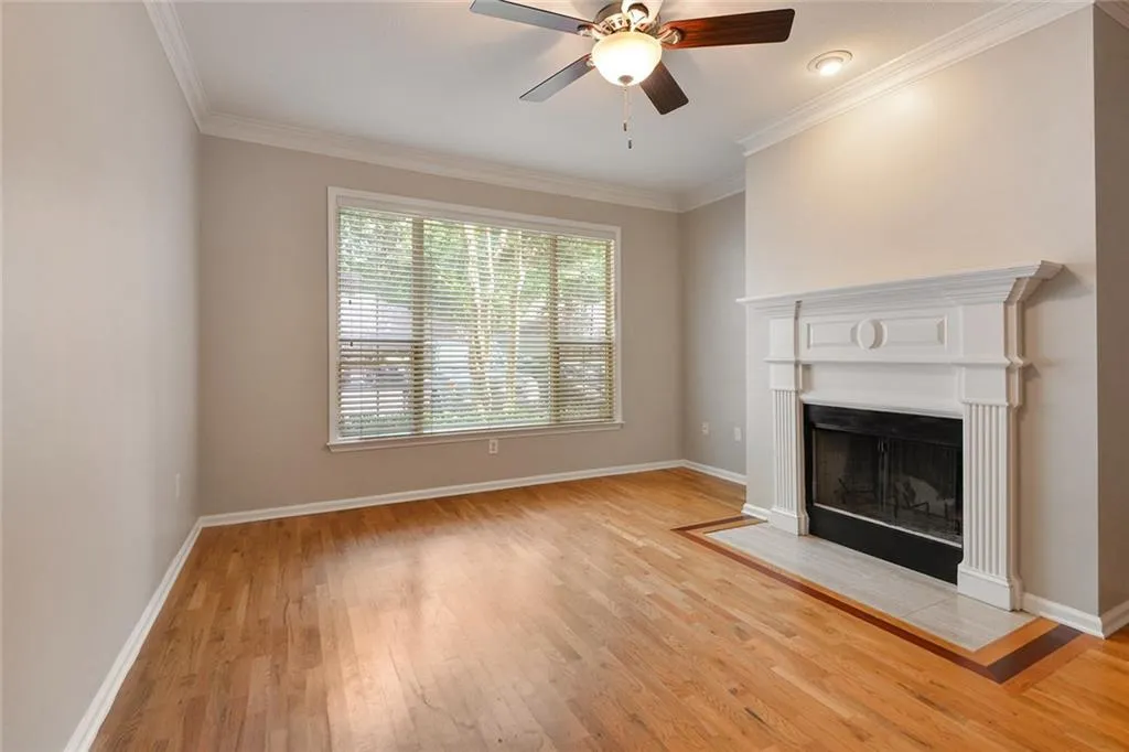 Unfurnished living room with crown molding, light wood-style flooring, a ceiling fan, and a fireplace with flush hearth