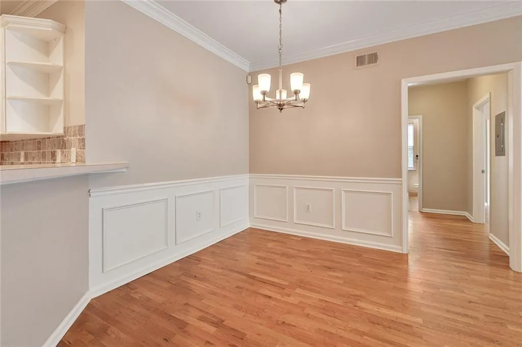 Unfurnished dining area with ornamental molding, a decorative wall, a wainscoted wall, a chandelier, and light wood-style flooring