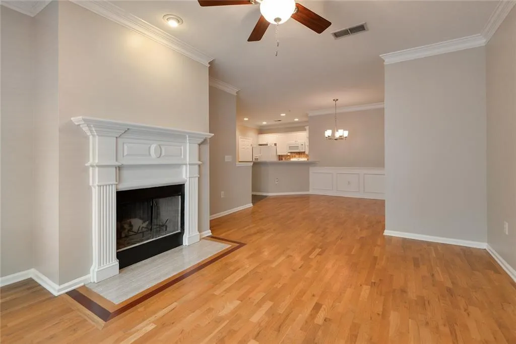 Unfurnished living room featuring ornamental molding, a ceiling fan, a chandelier, a fireplace with flush hearth, and light wood-style flooring
