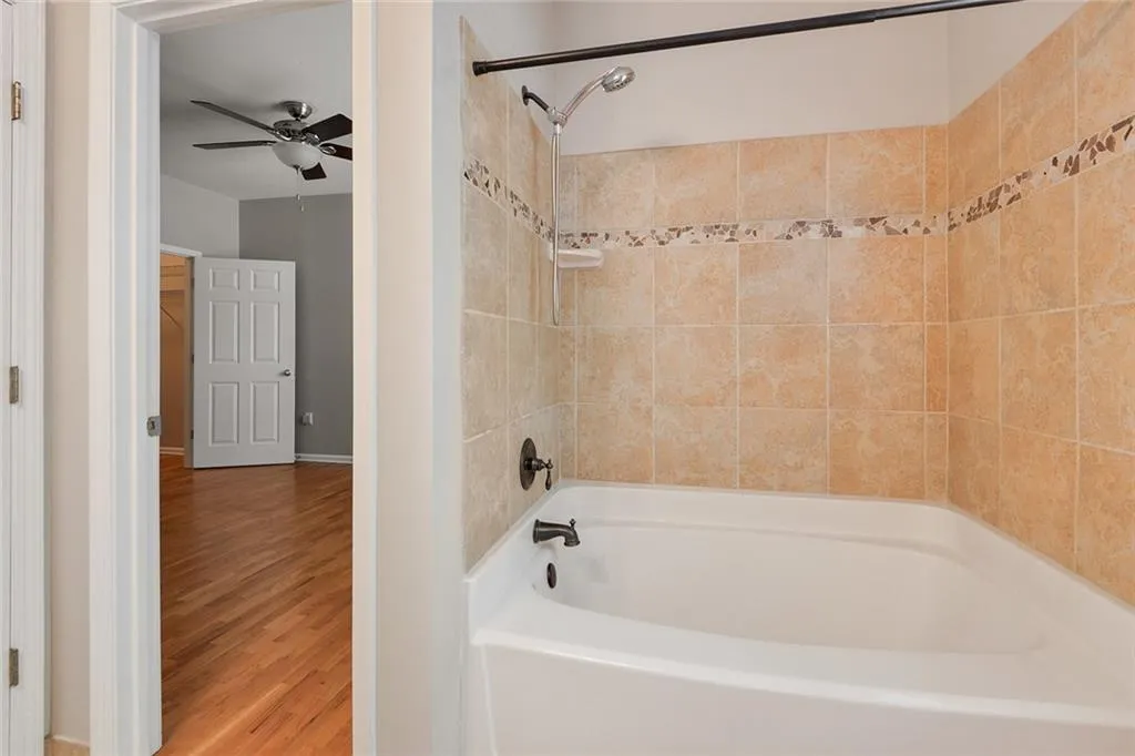 Bathroom featuring ceiling fan, wood finished floors, and shower / washtub combination