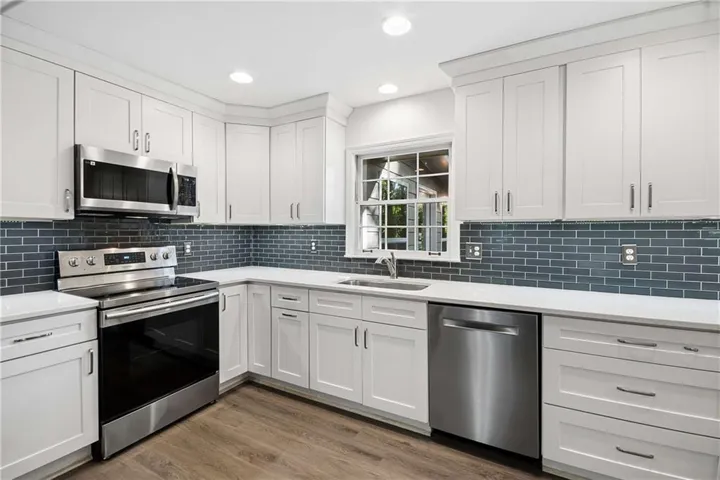 Modern kitchen featuring white shaker-style cabinetry, stainless steel appliances, a subway tile backsplash, white countertops, and wood-finish flooring