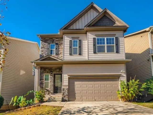 Two-story home with a stone and siding exterior, featuring a two-car garage, covered porch, and front landscaping