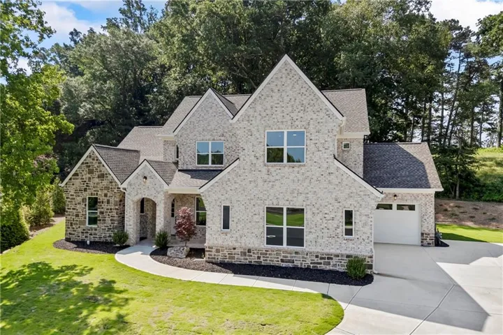 Stone and brick facade with multiple gables, an arched entryway, a concrete driveway, a two-car garage, and manicured landscaping