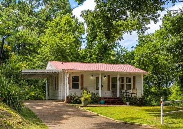 White siding exterior with a red metal roof, covered carport, and a front porch with dark wood-finish shutters