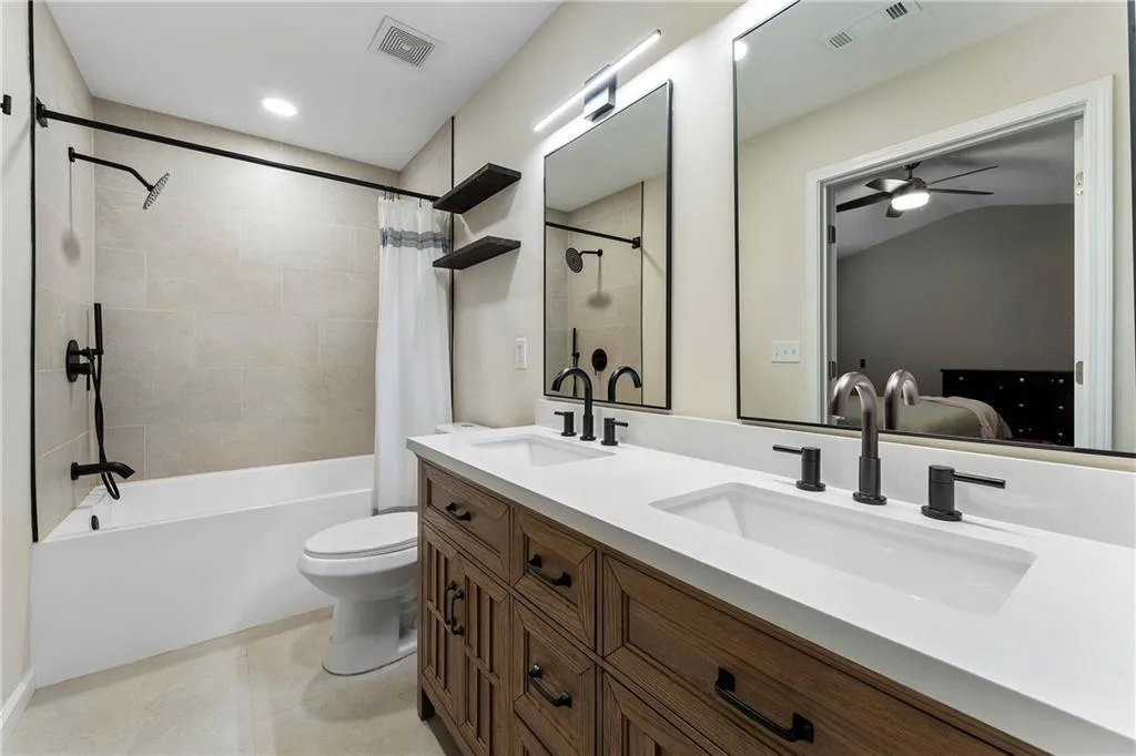 Ensuite bathroom featuring shower / bath combination with curtain, double vanity, ceiling fan, tile patterned floors, and vaulted ceiling
