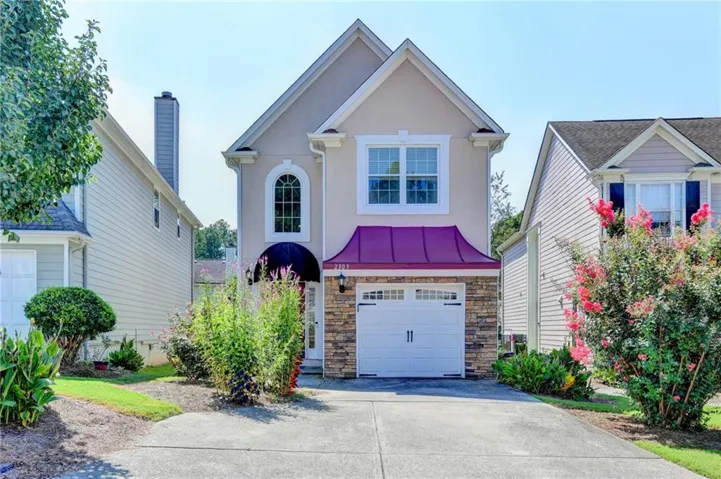 Stucco exterior with stone veneer accents, arched window, attached garage, and a curved metal awning