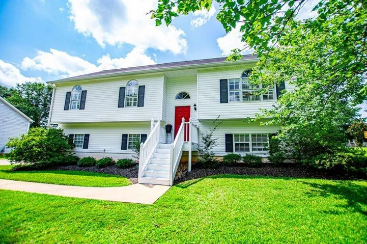 Split-level residence featuring white siding, black window shutters, an arched transom window, and a red entry door