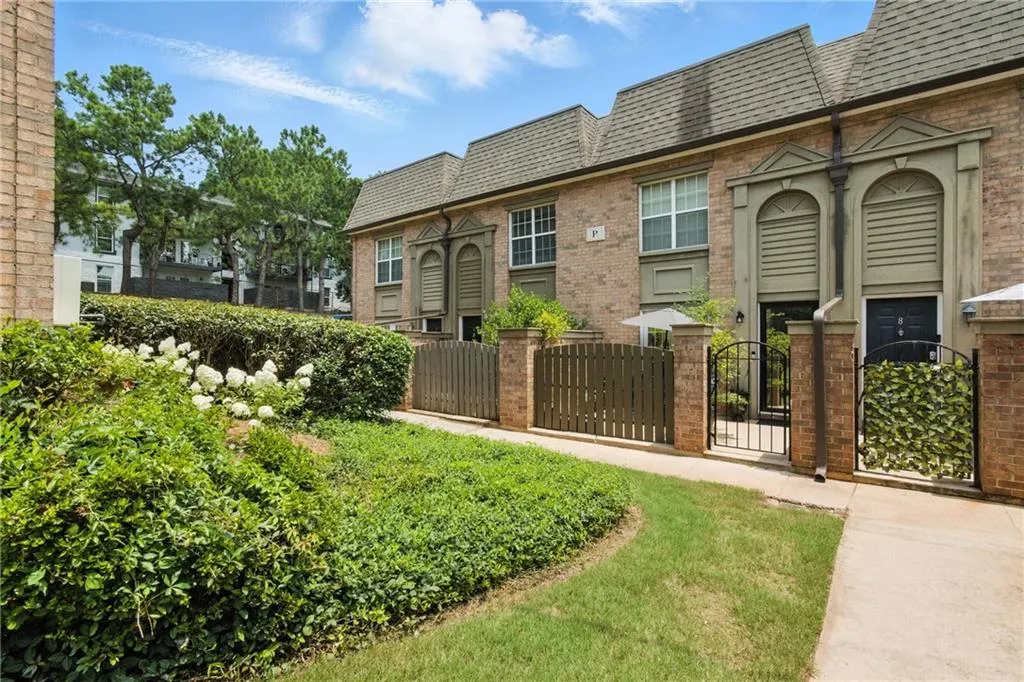 View of front of property with a fenced front yard, a gate, brick siding, mansard roof, and a shingled roof