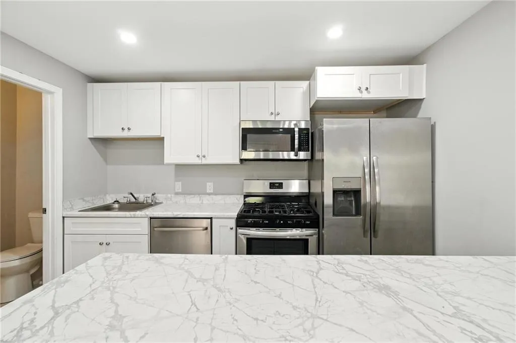 Kitchen with white cabinets, stainless steel appliances, and light stone countertops