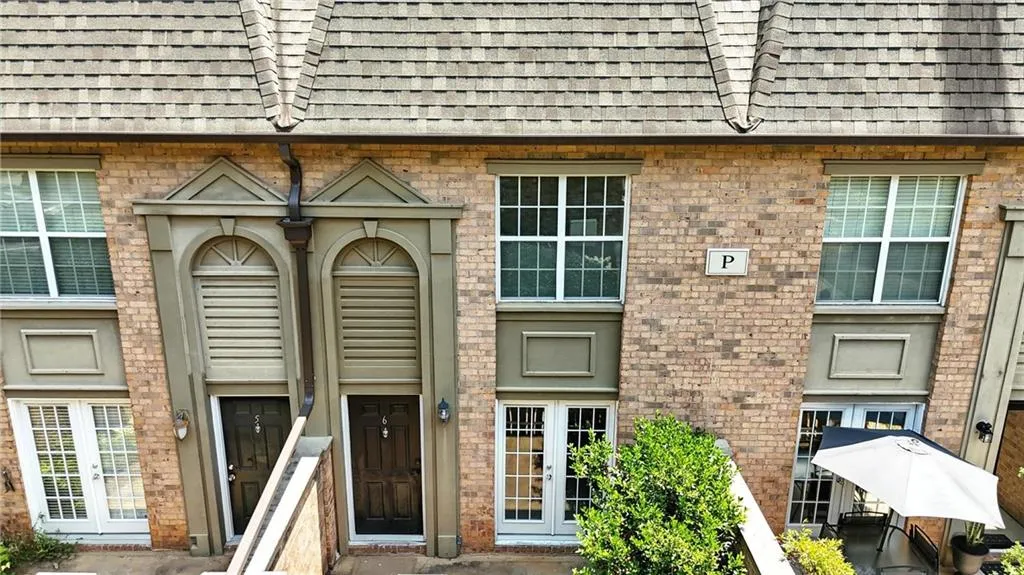 View of exterior entry featuring roof with shingles, mansard roof, brick siding, and french doors