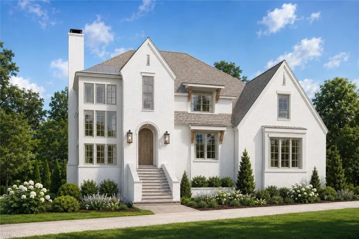 White brick exterior with a prominent chimney stack, multiple gabled rooflines, an arched wooden entry door, and exterior sconce lighting