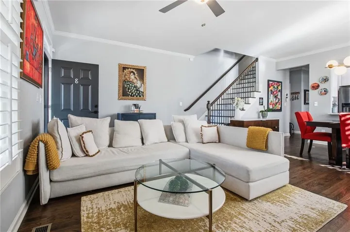 The open concept living area features hardwood flooring, a ceiling fan, and a staircase with dark wood handrails