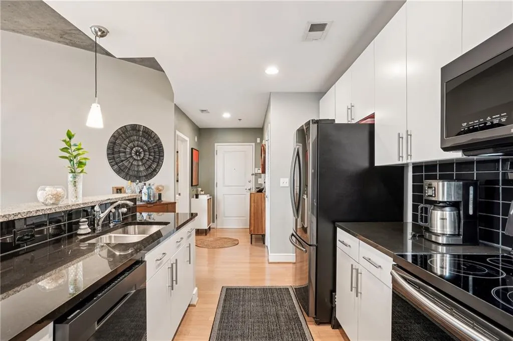 Kitchen featuring decorative light fixtures, white cabinetry, stainless steel appliances, dark stone counters, and light wood-style floors