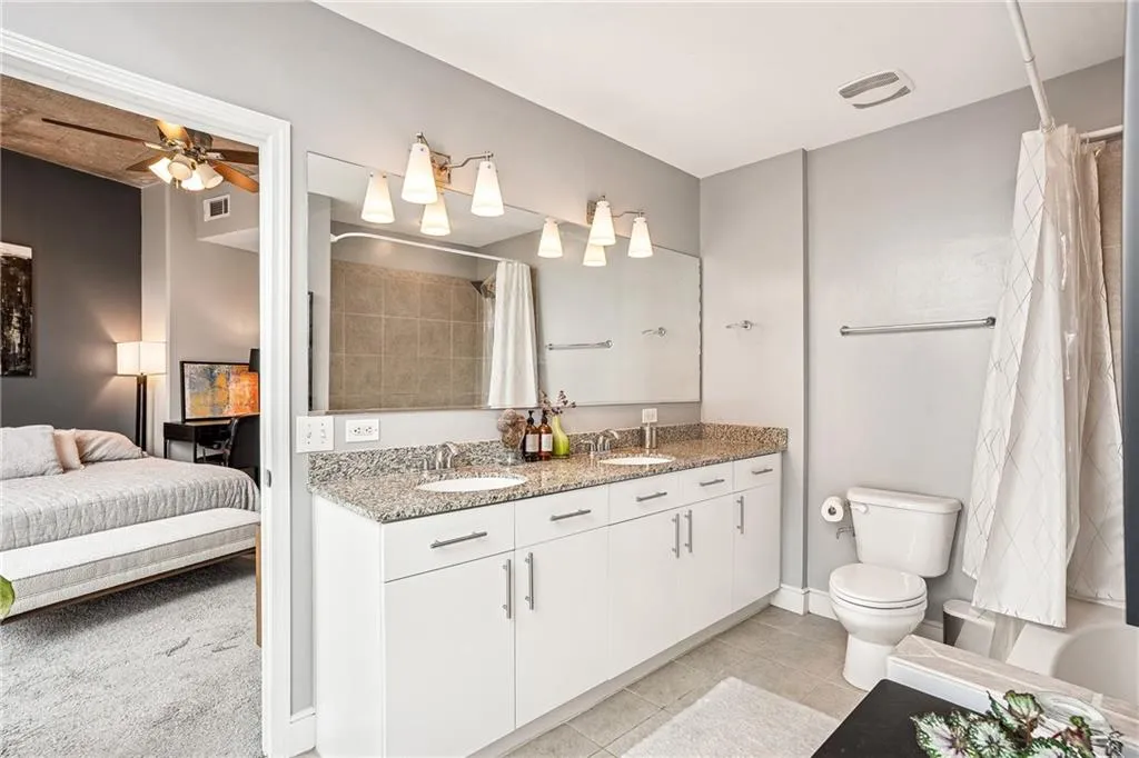 Ensuite bathroom featuring double vanity, light tile patterned floors, and a ceiling fan