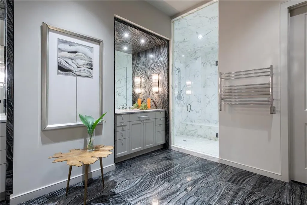 Primary bathroom featuring heated floors, towel warmer, walk-in steam shower, and dual vanities