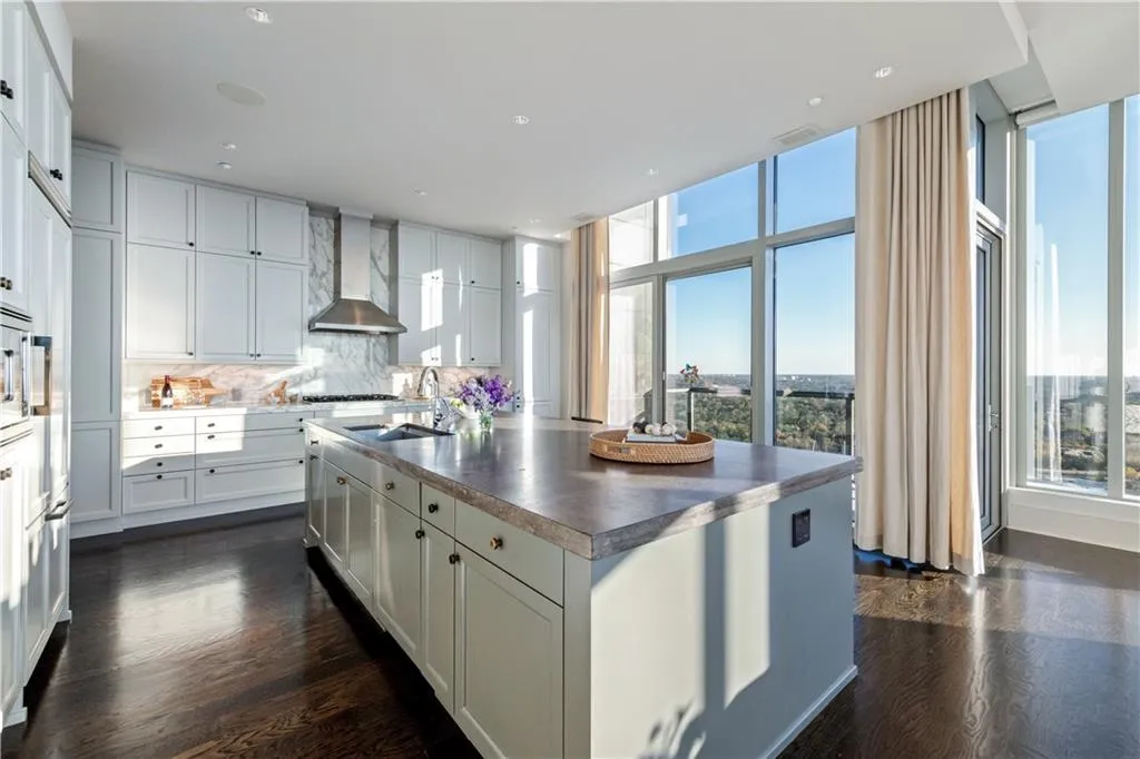 Kitchen featuring sink, a center island with sink, a wealth of natural light, wall chimney range hood, and white cabinets