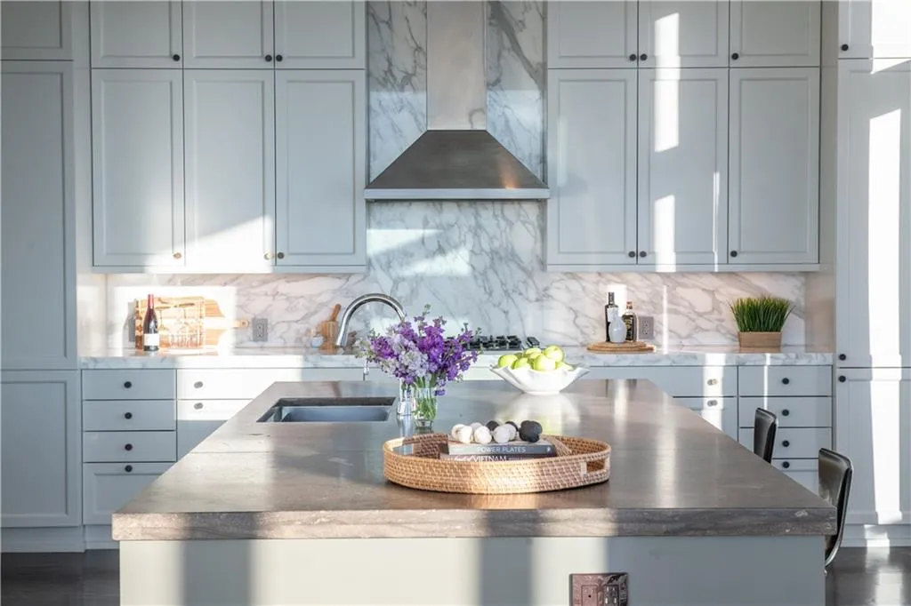 Kitchen featuring wall chimney range hood, decorative backsplash, and sink