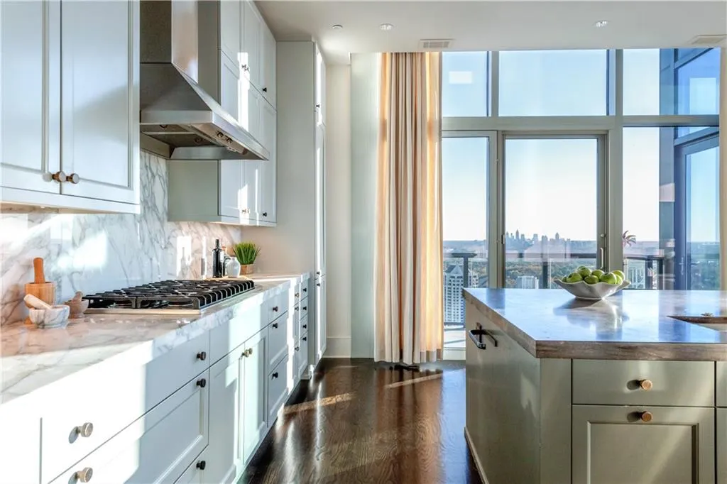 Kitchen featuring white cabinetry, light stone countertops, stainless steel gas stovetop, range hood, and backsplash