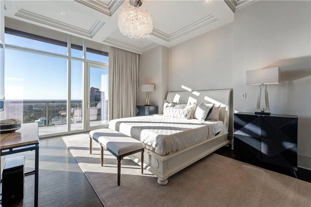 Primary bedroom featuring ornamental molding, coffered ceiling, access to balcony, and an inviting chandelier